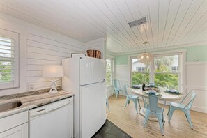 A kitchen with white cabinetry, a white refrigerator, and a dining area with light blue chairs and a round table.