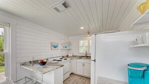 Une cuisine de taille réduite avec des meubles blancs, une cuisinière blanche et une poubelle bleue.