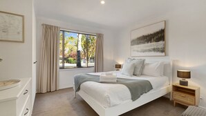 Un dormitorio con una cama grande, una mesita de noche, una ventana con cortinas y un cuadro en la pared.