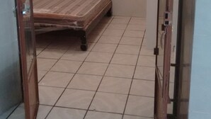 A room with a bed under a wooden archway, tiled floor, and a door.