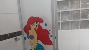 A bathroom with a toilet, a shower, and a wall with a mermaid mural.