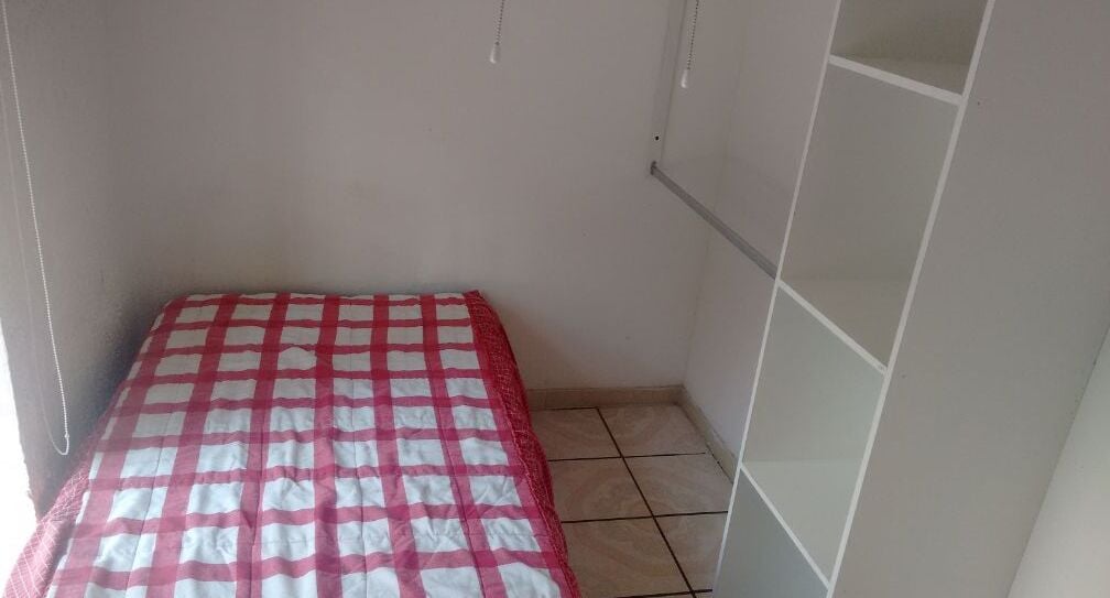 A small, narrow room with a checkered bedspread, tiled floor, and white walls.