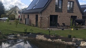 A two-story house with a sloped roof, a small pond, and a lawn.