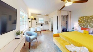 A compact hotel room with a bed, a TV, a desk, and a kitchenette.