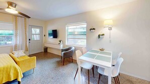 A compact room with a bed, a desk, a chair, a table, a TV, and a window.