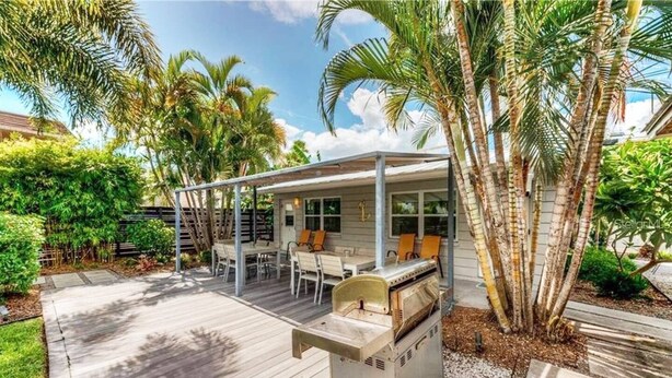 A covered outdoor patio with a grill, seating area, and palm trees.