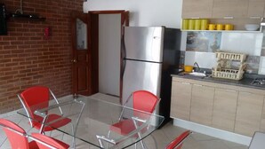 Eine Küche mit einem Edelstahlkühlschrank, einem Glastisch mit roten Stühlen und einer gefliesten Spritzschutzwand.