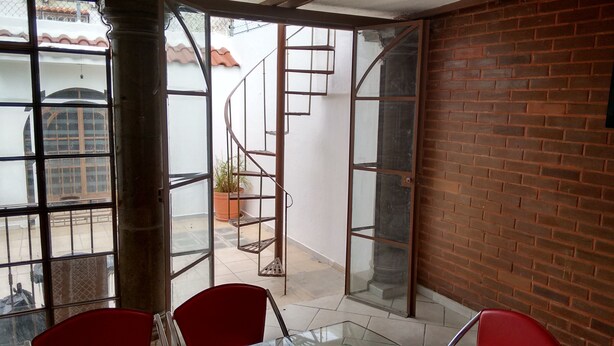 Ein Zimmer mit Glastür, die nach draußen führt, einer Ziegelwand und einer Wendeltreppe.