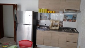 Eine kompakte Küche mit Edelstahlkühlschrank, Holzschränken, einem Gasherd und einem kleinen Spülbecken.