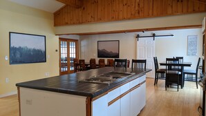 A spacious kitchen with a large island, wooden ceiling, and a dining area with chairs and a table.