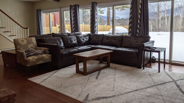 A living room with a sectional sofa, a small armchair, a coffee table, and a view of a snowy landscape through large windows.