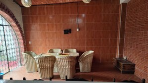 Un comedor con sillas de mimbre y una mesa, paredes de ladrillo y una ventana con barrotes.