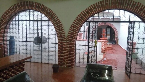 Una habitación con dos paredes de ladrillo en arco, suelo de baldosas y una reja de metal.