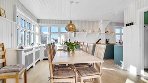Un comedor amplio con una mesa y sillas de madera, una lámpara colgante y ventanas grandes que dejan entrar luz natural.