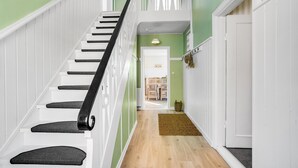 Una escalera con barandillas blancas y pasamanos negros que conduce a una habitación con pared verde y suelo de madera.