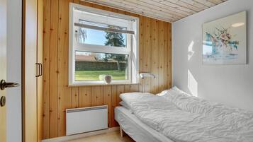 Une chambre avec un mur lambrissé en bois, une fenêtre avec des stores, un radiateur, un lit et une lampe fixée au mur.