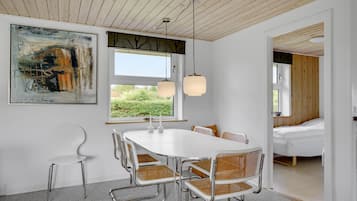 Un espace de salle à manger moderne avec une table et des chaises blanches, une grande peinture abstraite et une vue sur la verdure à l’extérieur.