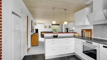 Une cuisine moderne avec des meubles blancs, un plafond en bois et des luminaires suspendus.