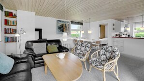 A modern living room with a black leather sofa, a wooden coffee table, and wicker chairs. There is a bookshelf filled with books and a painting on the wall. - 3 bedroom pet friendly home in Hejls (Hejls)