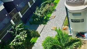 A rooftop garden with a solar panel, a pathway, and a building with a blue-tiled facade. - Stay here! Stay here! 2/4 furnished apartment in Costa Azul :-) (salvador)