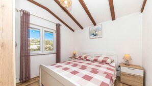 Ein Schlafzimmer mit einem Bett, zwei Nachttischen, einem Fenster mit Vorhängen, einem Bild an der Wand und Holzbalken an der Decke.