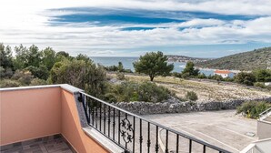 Ein Balkon mit Steinbalustrade, der auf eine Küstenlandschaft mit Bäumen und Meeresblick blickt.