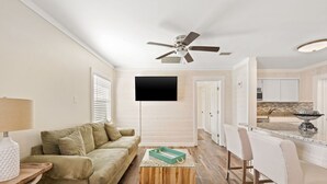 A modern living room with a sofa, a coffee table, and a TV mounted on the wall. - Pet Friendly House three minute walk to Beach! (Panama City Beach)