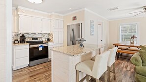 A modern kitchen with white cabinets, stainless steel appliances, a granite countertop, and a dining area with a wooden table and chairs. - Pet Friendly House three minute walk to Beach! (Panama City Beach)