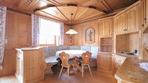 Interior de una cabaña de madera con una mesa de comedor, sillas, un banco y armarios de madera.