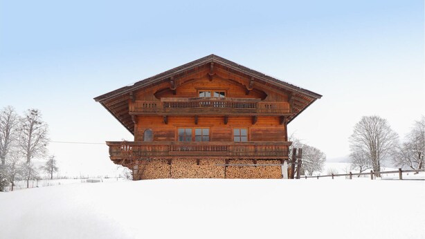 Una cabaña de madera con balcón, base de piedra y un paisaje nevado.