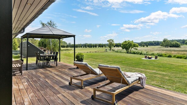 En træterrasse med en pergola, udendørs møbler og udsigt over en græsplæne.