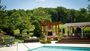 Piscina con pérgola y zona de estar al aire libre, rodeada de exuberante vegetación.
