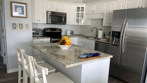 A modern kitchen with white cabinets, stainless steel appliances, and a granite countertop. - Coastal Condo w/ Ocean & Sound Views & Balcony (Emerald Isle)