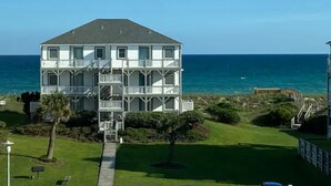 A two-story building with a balcony on the second floor, located near a body of water. - Coastal Condo w/ Ocean & Sound Views & Balcony (Emerald Isle)