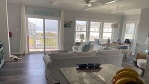 A spacious living area with a large window, a white sofa, and a kitchen counter with a fruit bowl. - Coastal Condo w/ Ocean & Sound Views & Balcony (Emerald Isle)