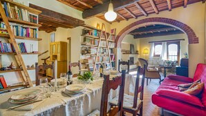 A cozy living room with a dining area, wooden bookshelves, a red sofa, and a brick fireplace. - 3 bedroom gorgeous home in Greve in Chianti (Greve in Chianti)