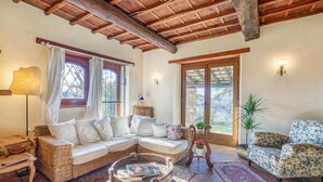 A cozy living room with a wicker sofa, a round coffee table with books, a floral armchair, and a view of the outdoors through a large window. - 3 bedroom gorgeous home in Greve in Chianti (Greve in Chianti)