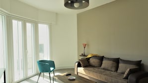 A modern living room with a sofa, a coffee table, and a chair. There is a large window providing natural light and a view outside. - T2 Liberté 3 minutes from beaches, shops and train station (Saint-Raphaël)