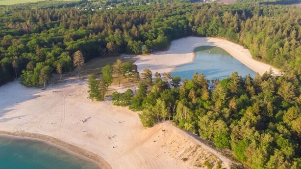 Vista aerea di una zona costiera con spiaggia sabbiosa, un piccolo lago e fitta vegetazione.