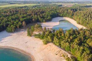 An aerial view of a coastal area with a sandy beach, a small lake, and dense forest.