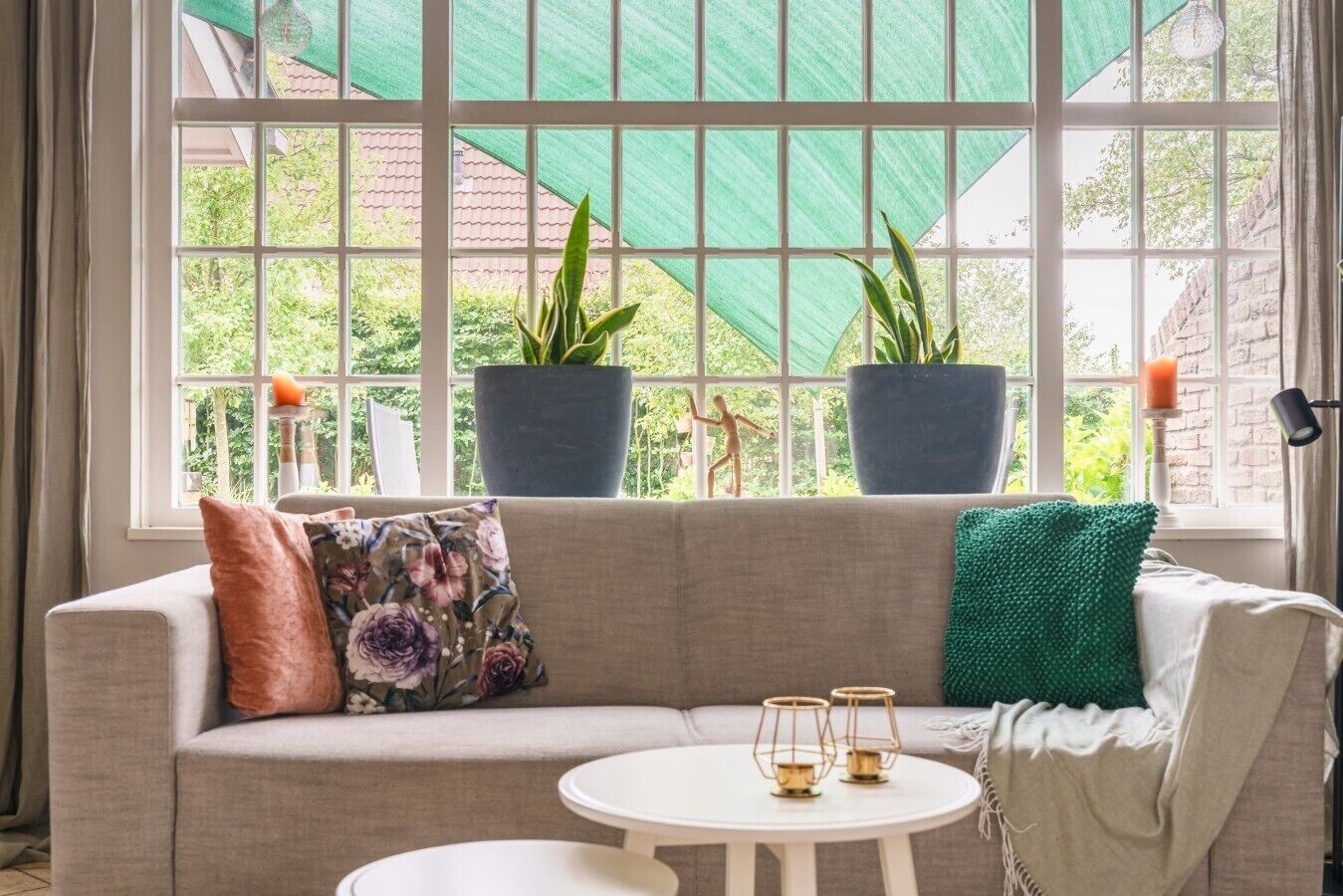 Une pièce comprenant un canapé, deux plantes en pot, une petite table ronde et une fenêtre donnant sur un paysage verdoyant.