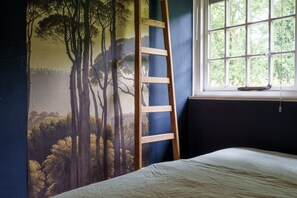 Une chambre à coucher avec un lit, une fenêtre et un mur orné d’une fresque représentant une forêt.