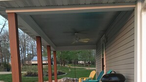 A covered porch with two chairs and a grill.
