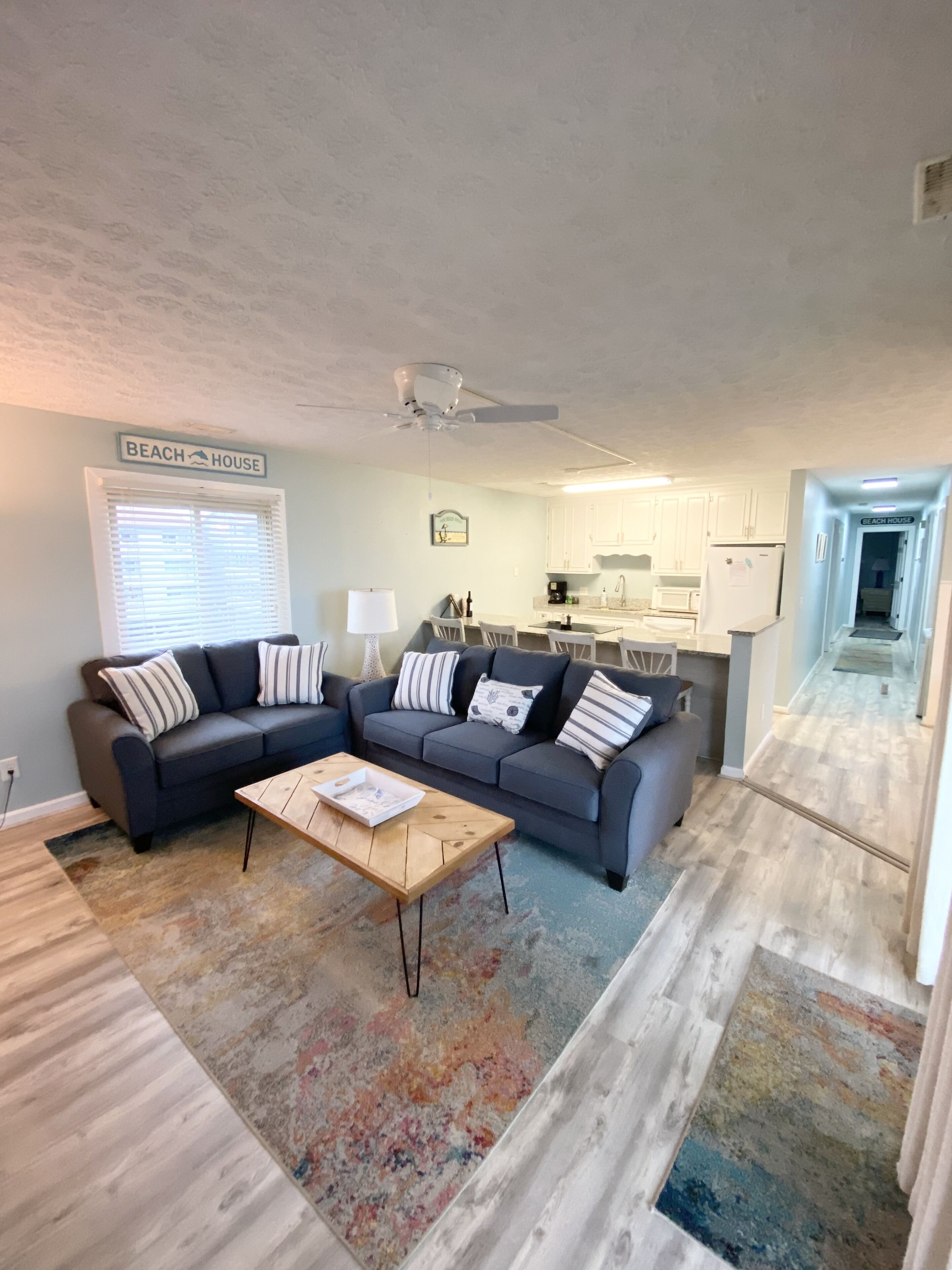 A living room with a sofa, coffee table, and a kitchen in the background.