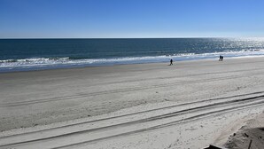 Une vaste plage, sous un ciel dégagé et avec une mer calme.