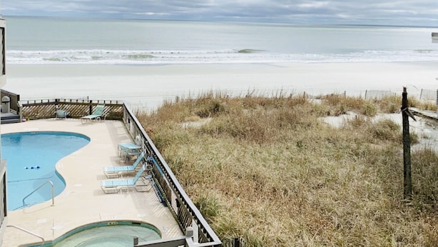 Un espace piscine avec des chaises longues et une vue sur la plage et l’océan.