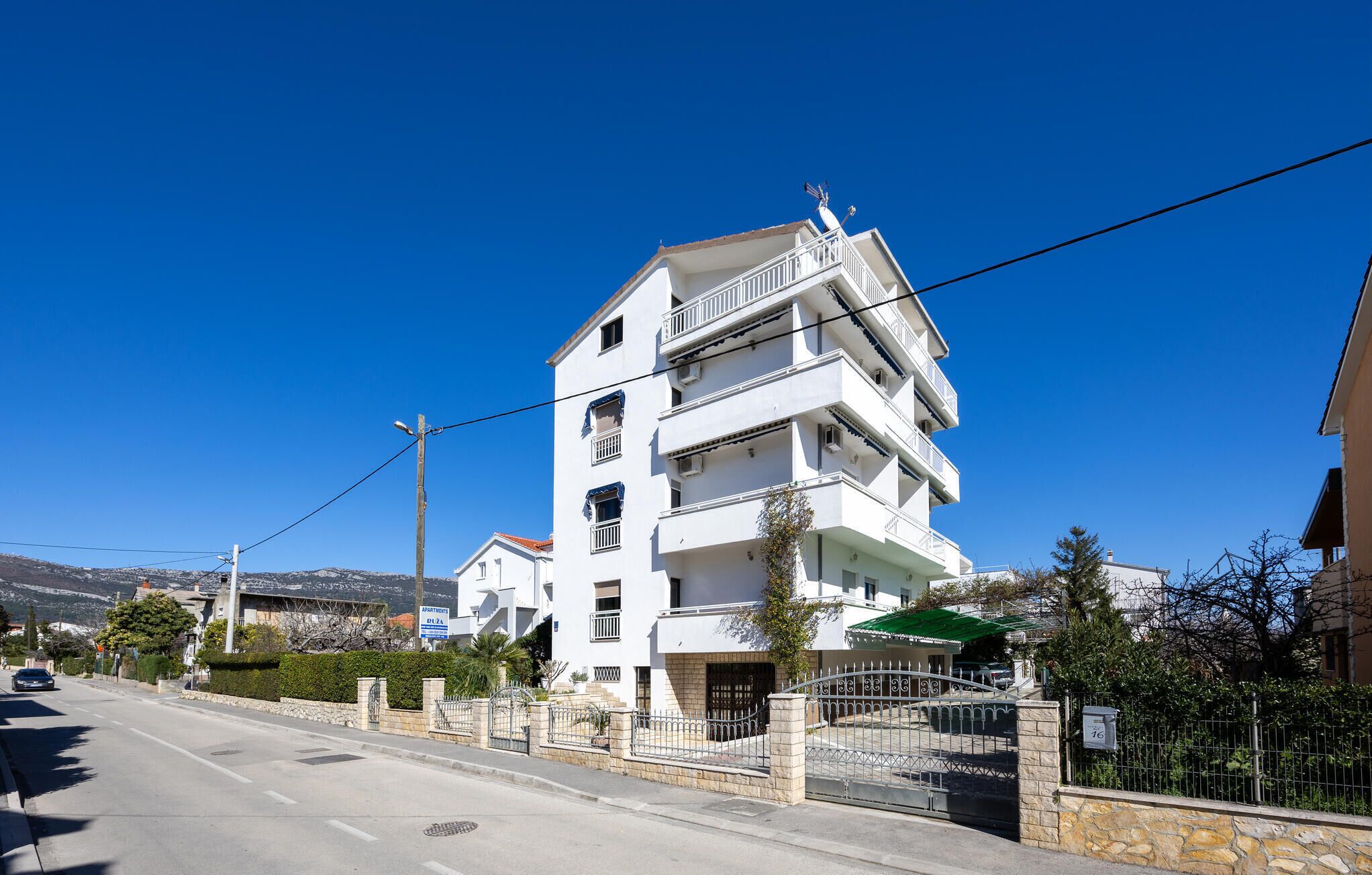A multi-story white building with balconies, a gated entrance, and a clear blue sky.