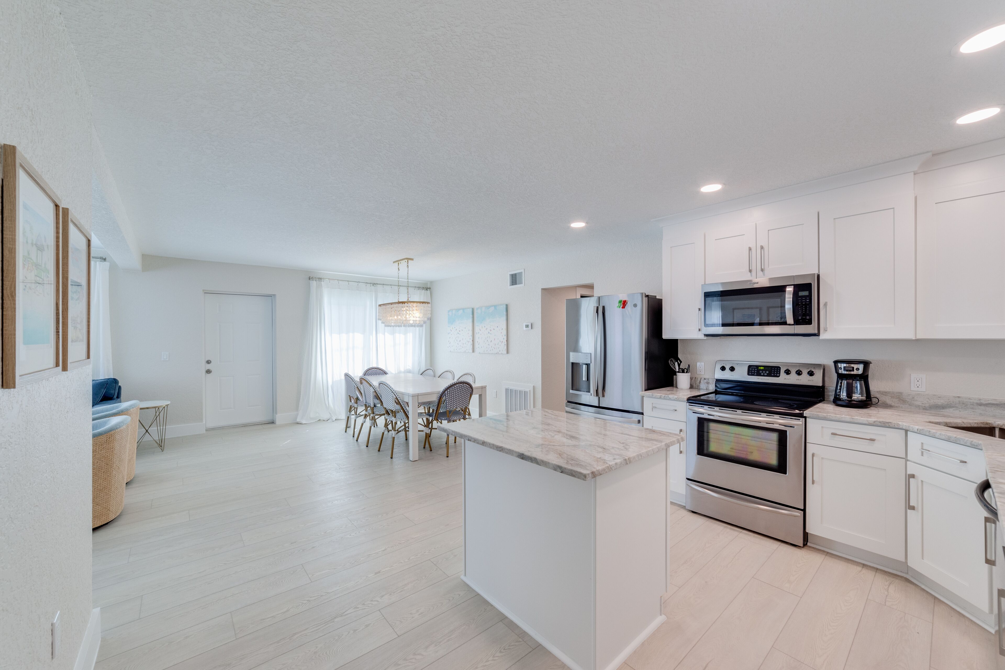 A modern kitchen with white cabinetry, a central island, stainless steel appliances, and a dining area with a table and chairs.