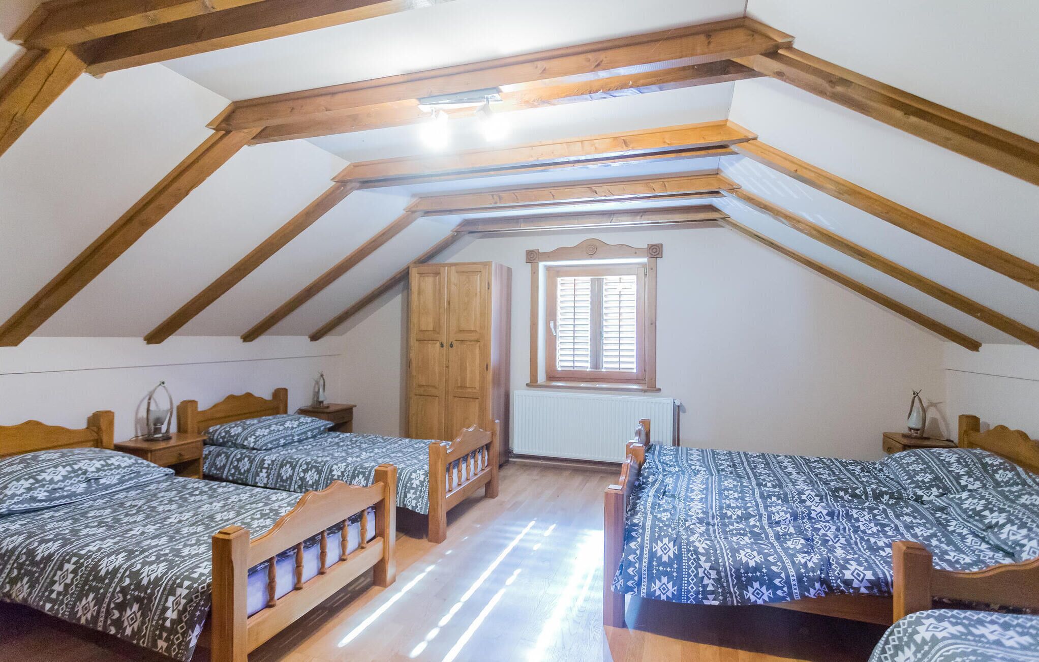 Una habitación con dos camas de madera, un armario de madera, una ventana con contraventanas y un radiador.