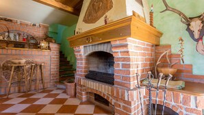 A rustic kitchen with a brick fireplace, wooden beams, and a checkered floor.